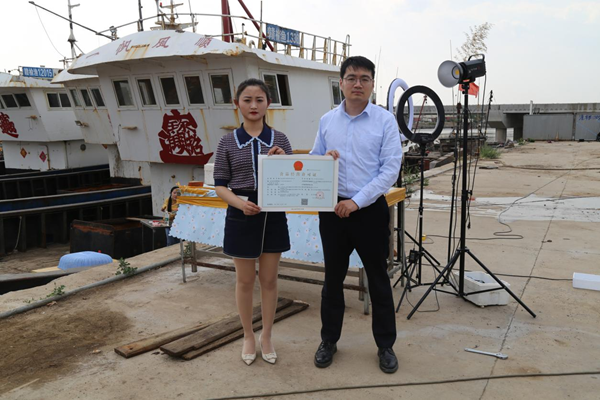 海鮮電商張夢琴與幫辦員手持食品經(jīng)營許可證合影。贛榆區(qū)委宣傳部供圖