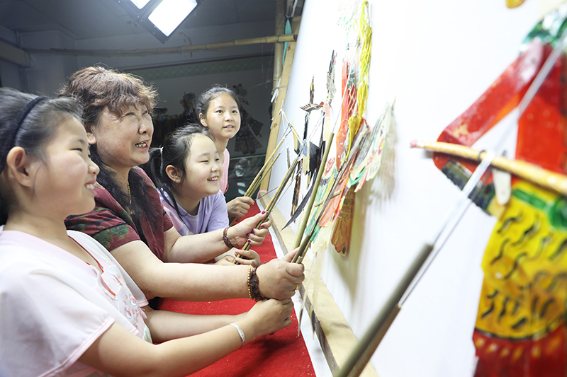 皮影藝人指導(dǎo)小朋友表演皮影戲。