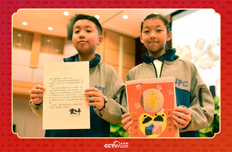 圖為香港“少年警訊”成員郭宏晞（左）展示習(xí)主席回信、羅顥凝（右）展示送給習(xí)主席的賀卡并合影。